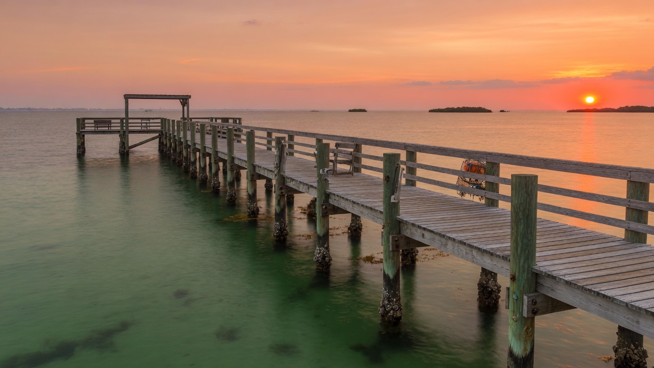 Wooden fishing pier over calm green Gulf of Mexico water at sunset near Pensacola Florida